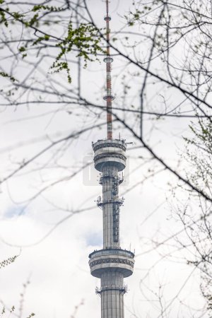 view of tv-tower through the tree branches. antenna-mast structure in the form of tower on which antennas for television transmitting station and radio broadcasting are installed. Tall large building