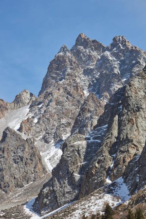 escarpado pico de montaña dentada se encuentra bajo el cielo azul claro. pico está parcialmente cubierto de nieve, lo que indica una gran altitud, bajas temperaturas. ausencia de vegetación, ubicación inaccesible. formaciones rocosas
