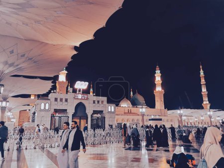 Photo for MEDINA, SAUDI ARABIA- DEC 31, 2022: Evening view of Muslim pilgrims walk by after evening prayers in Al Madinah, Saudi Arabia.  Muted pastel color filter applied. - Royalty Free Image