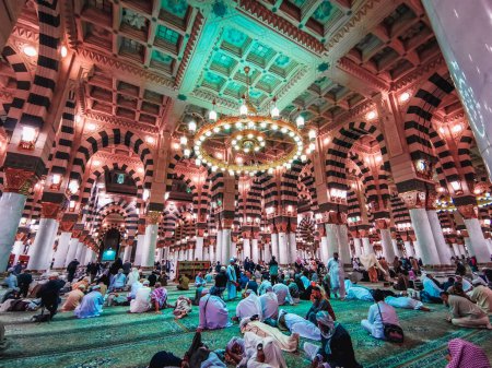 Photo for MEDINA, SAUDI ARABIA- JANUARY 1, 2023: Interior view of Muslim pilgrims relaxing after early morning prayer (salah) inside Nabawi mosque in Madinah, Saudi Arabia. Muted pastel color filter applied. - Royalty Free Image