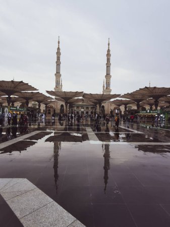 Photo for After rain reflection of Muslim pilgrims walking at the entrance of Nabawi mosque in Medina, Saudi Arabia. It is the second holiest mosque in Islam. - Royalty Free Image