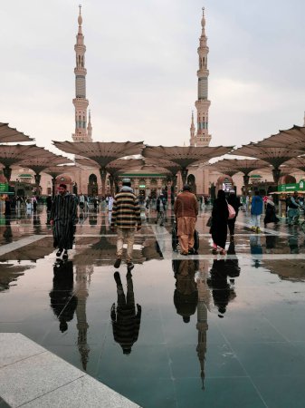 Photo for AL MADINAH, SAUDI ARABIA-JANUARY 2, 2023 : After rain reflection of Muslim pilgrims walking at the entrance of Nabawi mosque in Medina, Saudi Arabia. It is the second holiest mosque in Islam. - Royalty Free Image