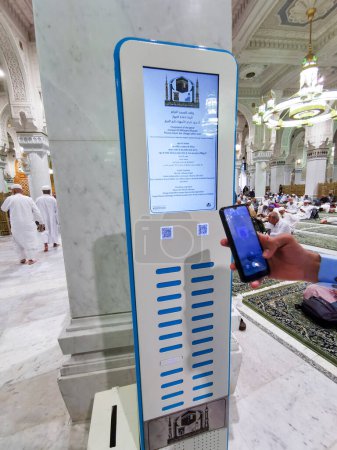 Photo for MECCA, KINGDOM OF SAUDI ARABIA-JUNE 1, 2023 : Unidentified man charges his smartphones inside Al Haram mosque in Makkah, Saudi Arabia. Mobile chargers kiosks were introduced here in early 2023. - Royalty Free Image