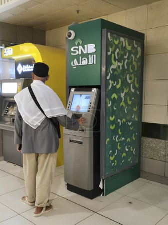 Photo for MECCA, KINGDOM OF SAUDI ARABIA-JUNE 4, 2023: An unidentified man withdraws money at Saudi National Bank (SNB) kiosk at Abraj Al Bait tower in Makkah, Saudi Arabia. - Royalty Free Image