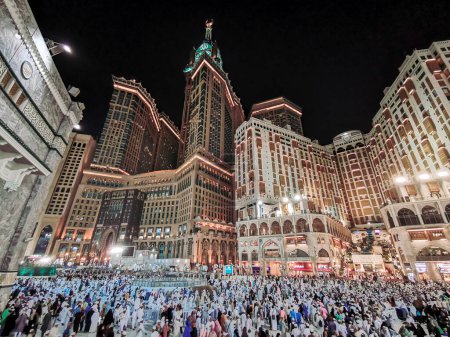 Photo for Muslim hajj pilgrims exit Al Haram mosque after evening prayers with Abraj Al Bait Zamzam tower (L) and Hilton Hotel Makkah (R) in the background. - Royalty Free Image