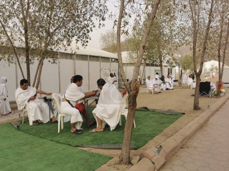 Téléchargez les photos : 26 JUIN 2023-PLAINE D'ARAFAT, MINA, ARABIE SAOUDITE : pèlerins malaisiens en vêtements blancs ihram se relaxant devant leur tente à la plaine d'Arafat à Mina, La Mecque, Royaume d'Arabie Saoudite. - en image libre de droit