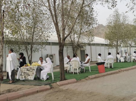 Téléchargez les photos : 26 JUIN 2023-PLAINE D'ARAFAT, MINA, ARABIE SAOUDITE : pèlerins malaisiens en vêtements blancs ihram se relaxant devant leur tente à la plaine d'Arafat à Mina, La Mecque, Royaume d'Arabie Saoudite. - en image libre de droit