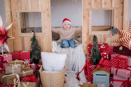 Téléchargez les photos : Petit garçon au chapeau de Père Noël jouant dans sa chambre d'enfant. Chambre décorée pour les vacances de Noël. - en image libre de droit