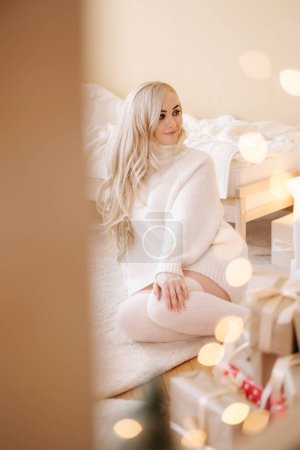 Téléchargez les photos : Portrait de Belle femme aux cheveux blonds en pull ouvert présent sur le temps de Noël. Femme élégante par arbre de Noël. Attrayant femelle tenir présent. L'humeur de Noël. Vacances d'hiver. - en image libre de droit
