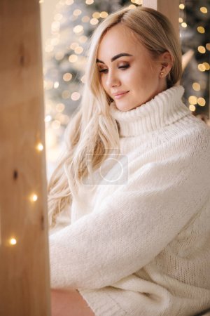 Téléchargez les photos : Portrait de Belle femme aux cheveux blonds en pull oversize ouvert présent sur le temps de Noël. Femme élégante par arbre de Noël. Attrayant femelle tenir présent. L'humeur de Noël. Vacances d'hiver. - en image libre de droit