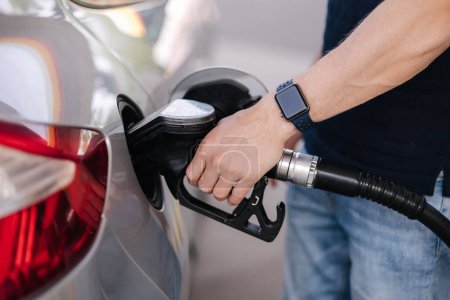 Close-up of young man refuelling a car at a petrol station. Middle selection of human hand hold fuel pump. High quality photo