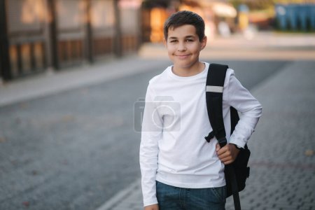 Porträt eines fröhlich lächelnden Teenagers in weißem Sweatshirt mit Rucksack draußen.