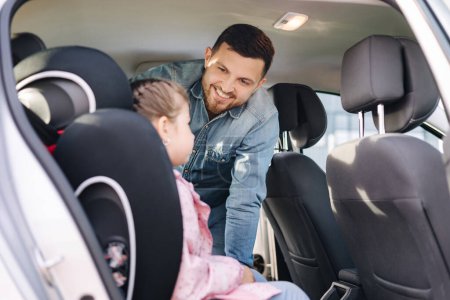 Photo for Handsome father put her daughter in a car seat and fastens her seat belts. Protection during the trip in the car. High quality photo - Royalty Free Image