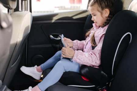 Photo for Adorable little girl using tablet in car on car seat. Trip . High quality photo - Royalty Free Image