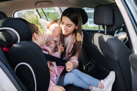 Photo for Attractive young mother put her daughter in a car seat and fastens her seat belts. Woman care about kid. Protection during the trip in the car. High quality photo - Royalty Free Image