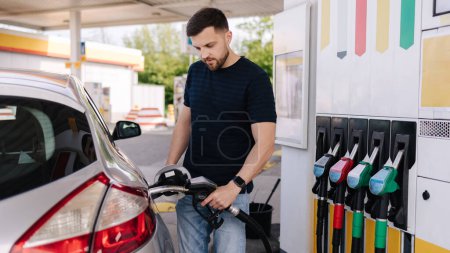 Foto de Un joven guapo repostando coche en la gasolinera. Diésel de llenado femenino con gasolina en el automóvil usando una boquilla de combustible. Concepto de gasolina. Vista lateral. Foto de alta calidad - Imagen libre de derechos