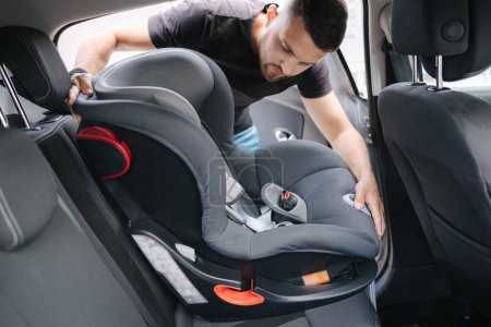 Man installs a child car seat in car at the back seat. Responsible father thought about the safety of his child. Man fasten seat belt on baby car seat.
