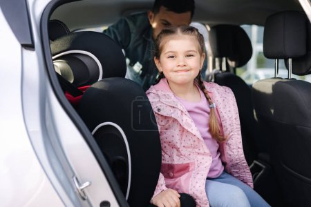 Photo for Handsome father put her daughter in a car seat and fastens her seat belts. Protection during the trip in the car. High quality photo - Royalty Free Image