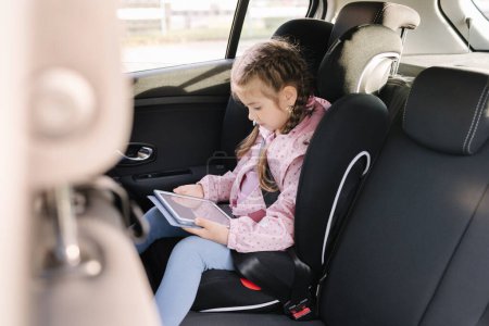 Photo for Cute little girl use tablet in car seat on the way to the kindergarten. High quality photo - Royalty Free Image