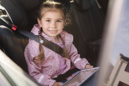 Photo for Adorable little girl using tablet in car on car seat. Trip . High quality photo - Royalty Free Image