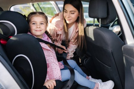 Photo for Attractive young mother put her daughter in a car seat and fastens her seat belts. Woman care about kid. Protection during the trip in the car. High quality photo - Royalty Free Image