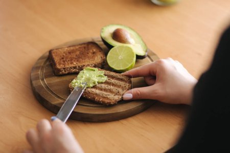 Woman spread guacamole on toasted dark bread. High quality photo