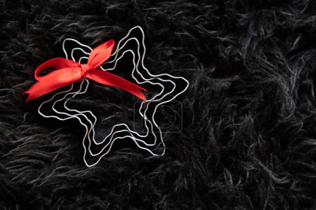 Foto de Decoración navideña en forma de estrella con cinta roja sobre fondo suave y oscuro. - Imagen libre de derechos