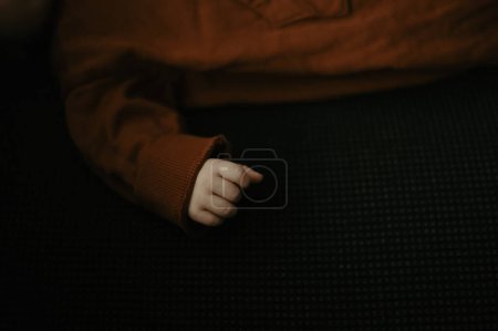 Foto de Closeup on newborn baby hand and fist. Baby dressed in warm brown clothing when lying on black cozy blanket. - Imagen libre de derechos