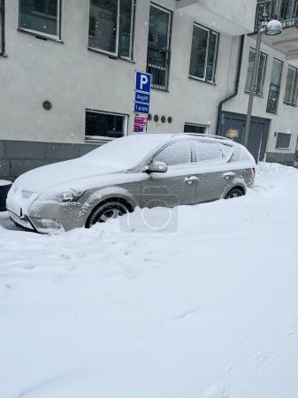 Foto de Estocolmo, Suecia - 8 de marzo de 2023: Coche cubierto de nieve después de una tormenta de nieve en la ciudad. Nieva en vehículo estacionado en la calle fuera del edificio residencial. Día de invierno nevando. - Imagen libre de derechos