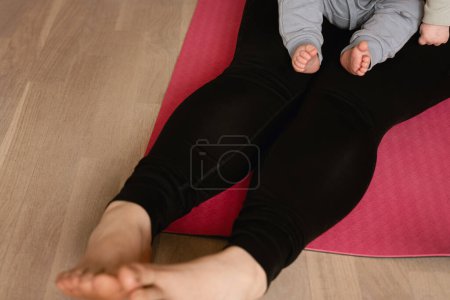Foto de Bebé y mujer sentados en una esterilla de yoga. Concepto de ejercicio posparto, entrenamiento con bebé o niño pequeño. Estilo de vida activo con entrenamiento después del parto. - Imagen libre de derechos
