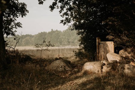 Foto de Paisaje rural durante la salida del sol en una mañana de verano. Antiguo muro de piedra, hierba, puerta de madera y campo de agricultura y bosque en el fondo. Foto tomada en el archipiélago de Karlskrona, Suecia. - Imagen libre de derechos