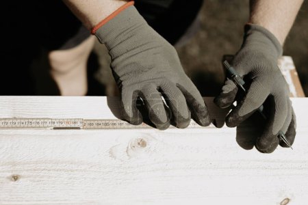 Foto de Primer plano de una persona que trabaja en un sitio con guantes protectores, midiendo la madera con la ayuda de un lápiz. Foto tomada en Suecia. - Imagen libre de derechos