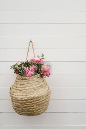 Foto de Hermosa decoración de flores colgando de la pared. Cesta con rosas rosadas y flores de verano colgando de la pared de madera blanca. Foto tomada en España. - Imagen libre de derechos
