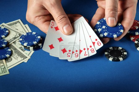 Foto de Jugador pone cartas de juego con escalera combinación ganadora en el juego de póquer en la mesa azul con fichas y dinero en el club - Imagen libre de derechos