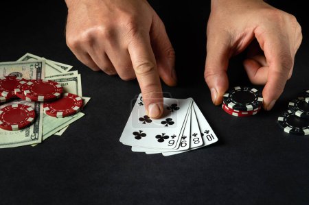 Photo for The player points with his finger at a winning straight flush combination in poker game on a black table with chips and money in club - Royalty Free Image