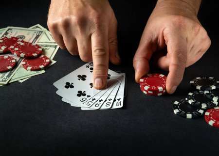 Foto de El jugador apunta con su dedo a una combinación de escalera ganadora en el juego de póquer en una mesa negra con fichas y dinero en el casino. - Imagen libre de derechos
