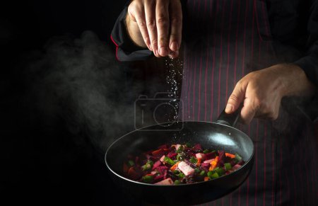 Photo for Cooking fresh vegetables. Chef adds salt to a steaming hot pan. The idea of European cuisine for a hotel with advertising space. - Royalty Free Image