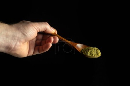 Mixture of dry ground herbs in a wooden spoon in a person hand before adding to tea. Free space for advertising on a black background
