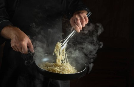Téléchargez les photos : Frites spaghetti chef professionnel dans une poêle chaude à la vapeur. Espace publicitaire sur fond noir. Plat national italien - en image libre de droit