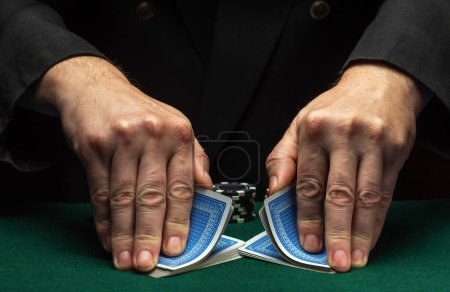 Foto de Quick shuffling of playing cards by the hands of an experienced dealer or croupier in a poker club on a green table with playing chips. Casino card game concept - Imagen libre de derechos