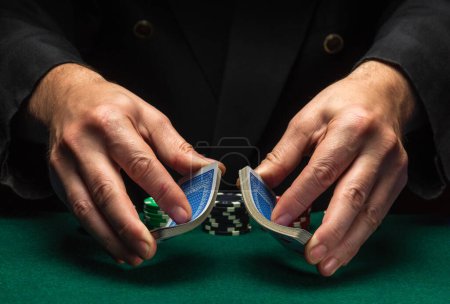 Foto de Distribuidor profesional o crupier baraja jugando a las cartas en un club en una mesa verde con fichas. El concepto de un exitoso juego de póquer en un casino. - Imagen libre de derechos