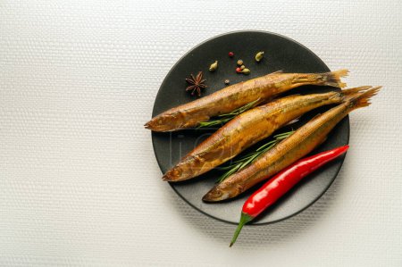 Photo for Smoked capelin on a dark plate with rosemary and pepper is served for lunch. Light space for advertising. - Royalty Free Image