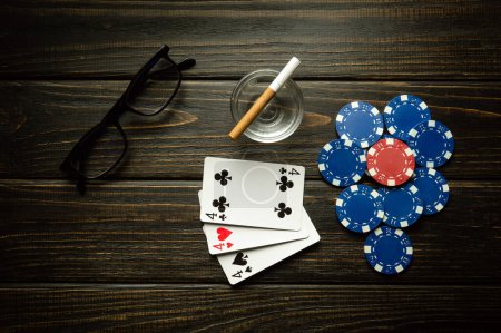 Photo for Playing cards with a winning combination of three of a kind or set and glasses with a cigarette on a black vintage table in a poker club. Winning in sports depends on luck. - Royalty Free Image