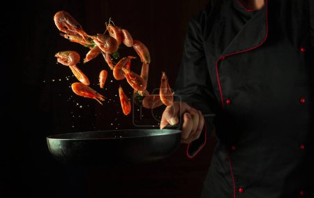 Photo for The cook prepares shrimps in a frying pan with parsley. The concept of cooking seafood and healthy vegetarian food on a dark background. - Royalty Free Image
