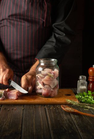 Photo for The chef cuts the fish into steaks before preparing the herring in a jar. Work environment on the kitchen table with aromatic spices. - Royalty Free Image