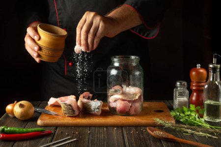 Photo for A chef salts steaks with raw fish before cooking herring in a jar. Concept of salting or canning fish - Royalty Free Image