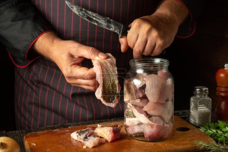 Photo for Cutting raw carp fish for preparing herring in a jar or canning. Knife in the hand of the cook and steak with fish. - Royalty Free Image