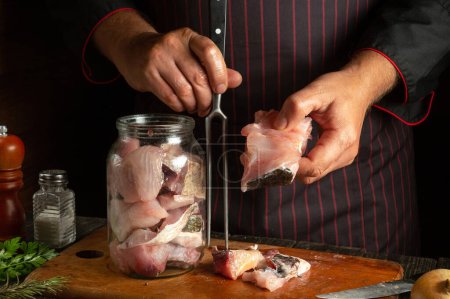 Photo for A cook fills a jar with fish steaks for canning or salting. Working environment on a restaurant kitchen table. - Royalty Free Image