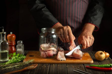 Photo for The cook cuts the raw fish into steaks and then cooks the herring in a jar. Working environment on the kitchen table with aromatic spices and pepper - Royalty Free Image
