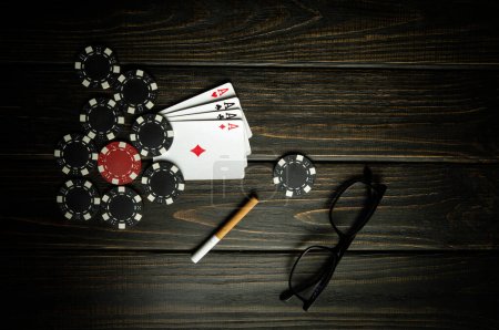 Foto de Un juego de póquer muy popular y de juego con una combinación ganadora de cuatro de un tipo o quads. Tarjetas con papas fritas y vasos con un cigarrillo en una mesa vintage negra en un club de poker. - Imagen libre de derechos